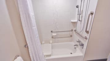 Une salle de bain avec une baignoire blanche, des barres d’appui, une pomme de douche et un porte-serviettes.
