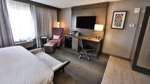 Une chambre d’hôtel avec un lit, un bureau et une chaise, une télévision et une fenêtre avec des rideaux.