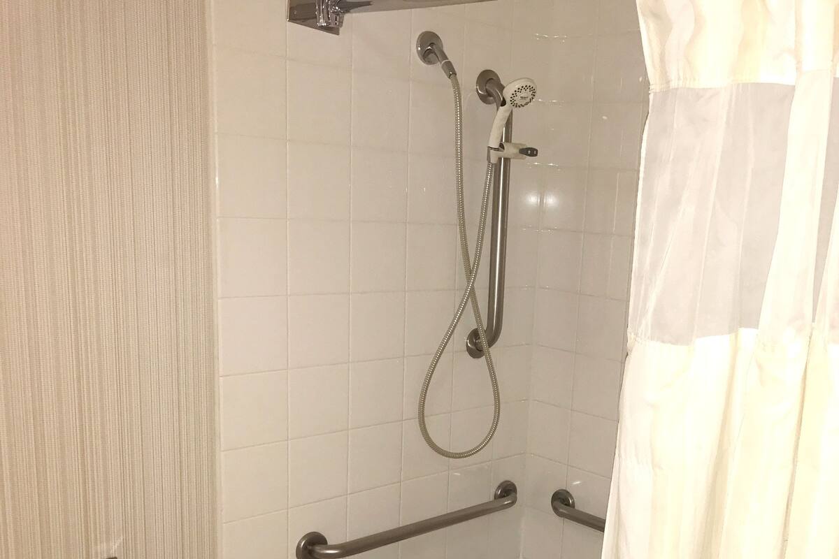 A bathroom with a bathtub, a shower, grab bars, and a towel rack.