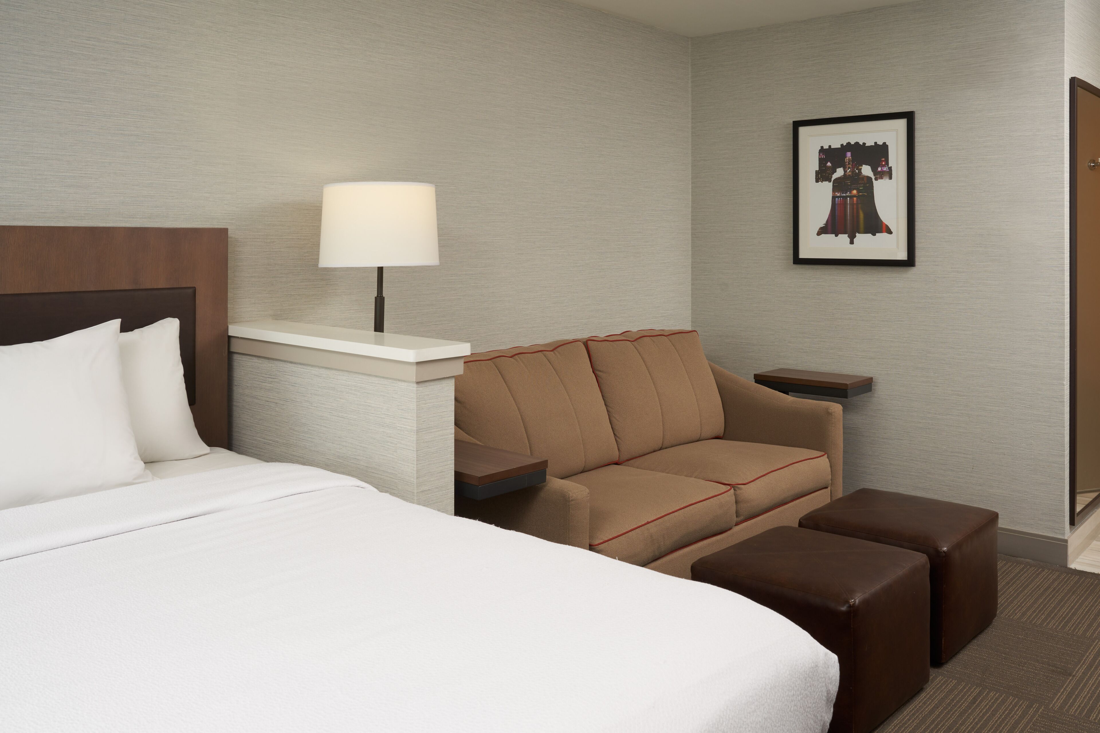 Una habitación de hotel con cama, sofá, mesa, lámpara y un cuadro en la pared.