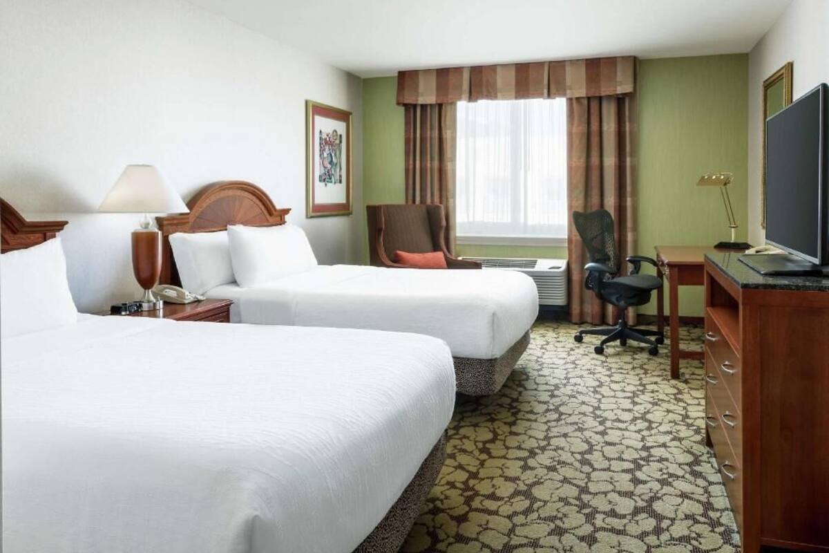 A hotel room with two beds, a desk, a chair, a television, and a window with curtains.