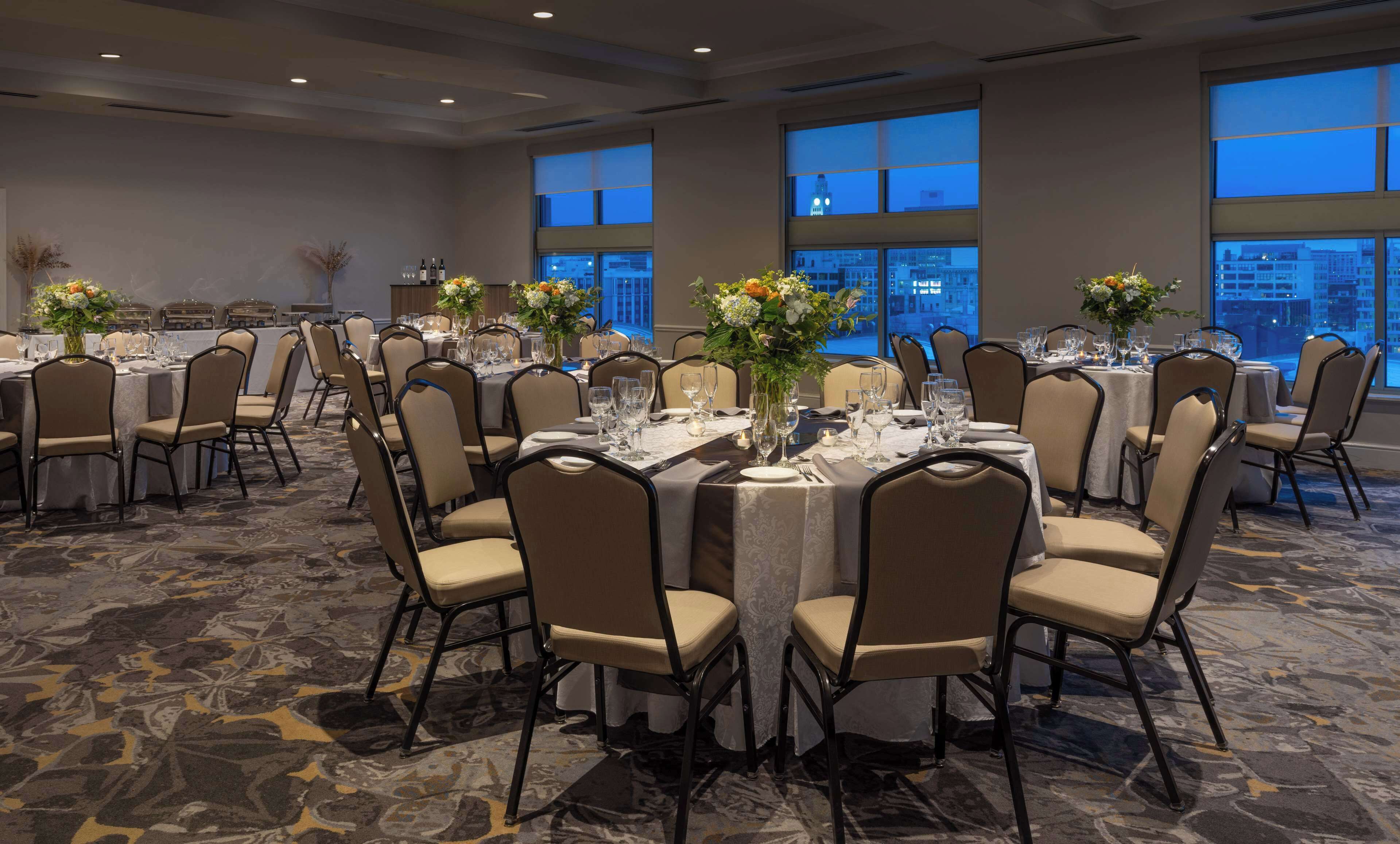 A banquet hall with round tables, chairs, and floral centerpieces.