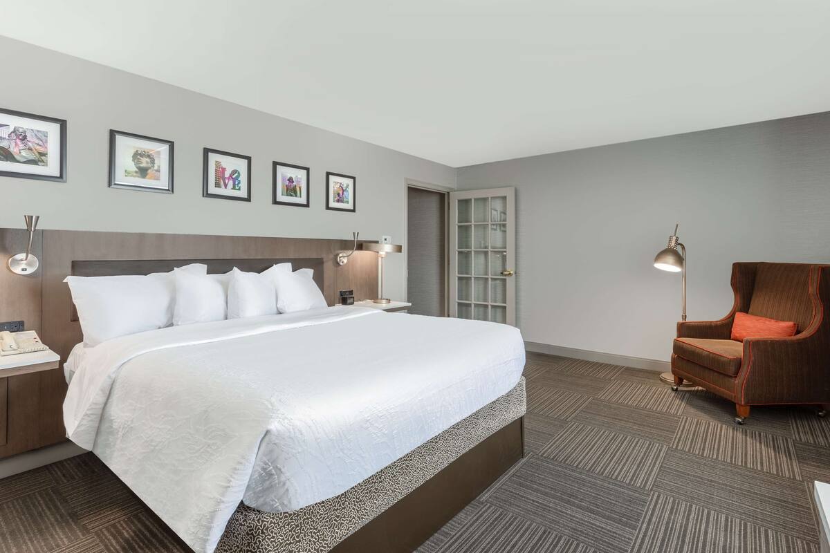 A hotel room with a large bed, a chair, a nightstand, a lamp, and framed pictures on the wall.