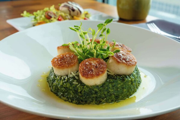 A plate of food with seared scallops and a green puree, garnished with microgreens.