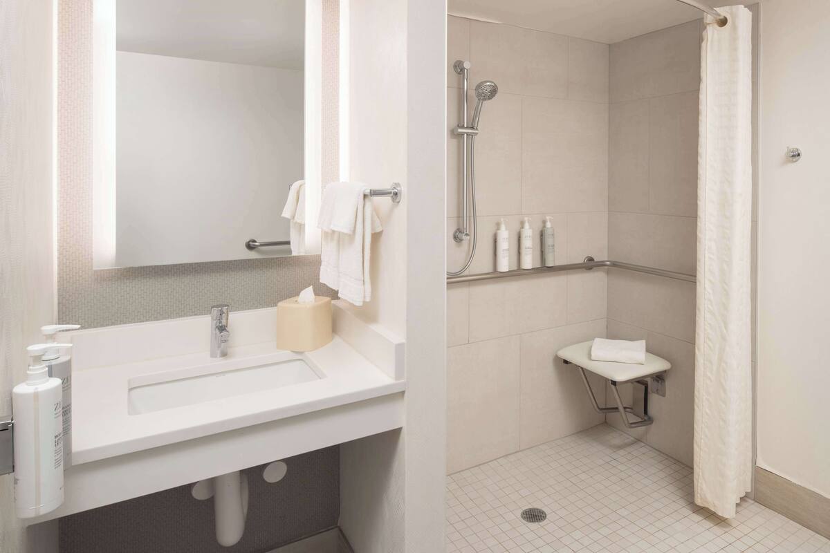A modern bathroom with a sink, mirror, towel rack, shower, and toilet.