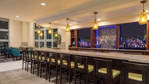 A bar area with a long counter, multiple stools, and a bar stocked with bottles. - Hilton Garden Inn Philadelphia Center City (Philadelphia)