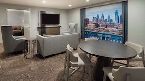 A hotel room with a cityscape view, a flat-screen TV, a sofa, a dining table with chairs, and a patterned carpet. - Hilton Garden Inn Philadelphia Center City (Philadelphia)