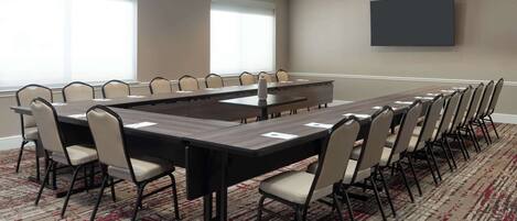 A conference room with a long table, chairs, a flat-screen TV, and large windows.