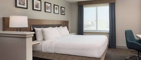 A hotel room with a large bed, a desk, a chair, and a window with curtains.