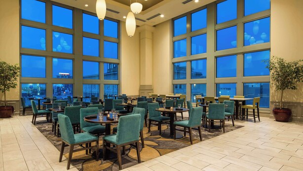 A spacious hotel lobby with large windows, multiple dining tables, and green upholstered chairs. - Hilton Garden Inn Philadelphia Center City (Philadelphia)