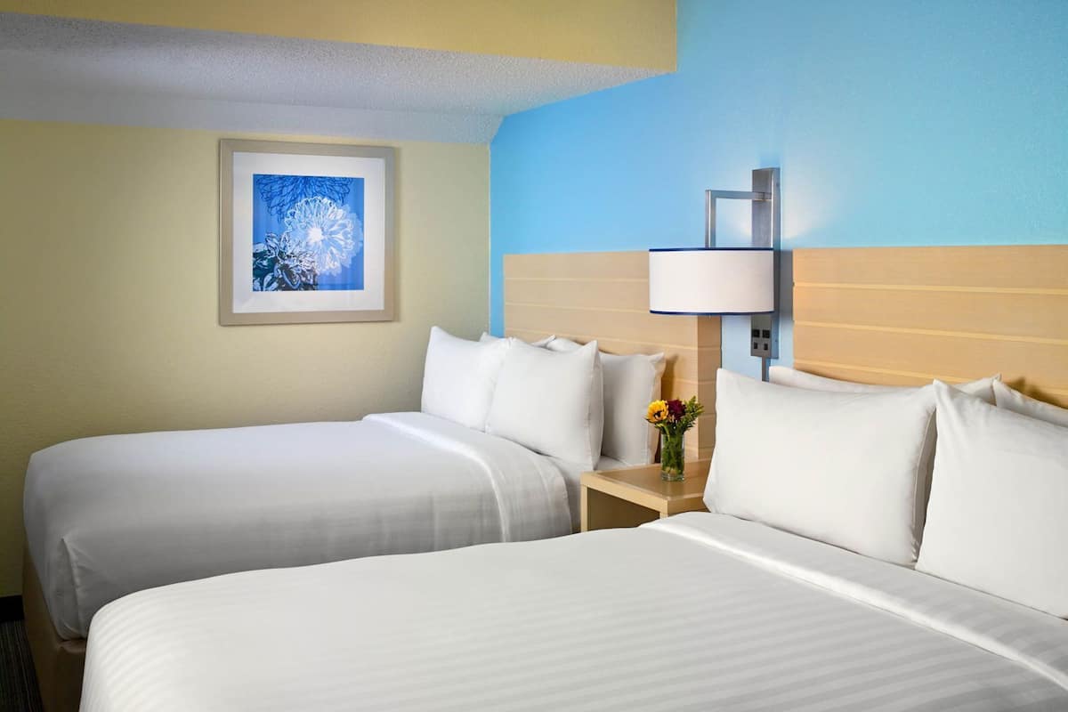 Una habitación de hotel con dos camas, una mesita de noche con una lámpara y un cuadro en la pared.