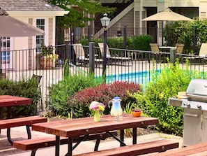 A poolside patio with wooden tables and benches, surrounded by greenery and a barbecue grill. - Sonesta ES Suites Charlotte Arrowood (Charlotte)