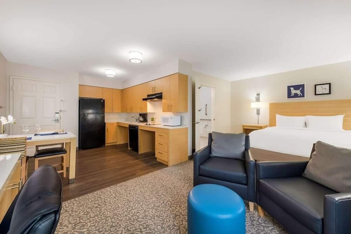 Habitación de hotel con cama, escritorio, silla, sofá, zona de cocina y baño.