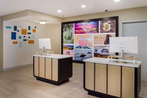 A reception area with two reception desks, a wall with abstract art, and a large poster with various images. - Sonesta ES Suites Charlotte Arrowood (Charlotte)