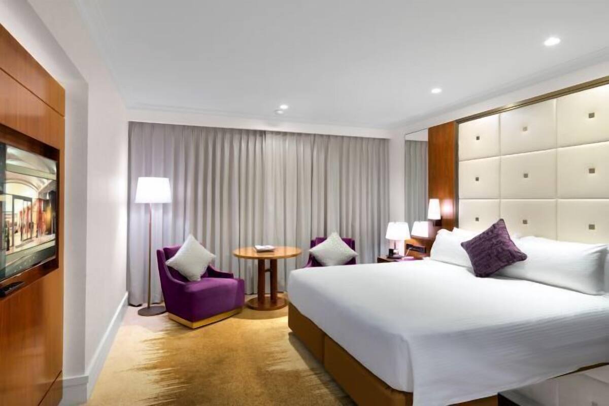 Ein Hotelzimmer mit einem großen Bett, zwei Sesseln, einem kleinen Tisch und einem Fernseher.