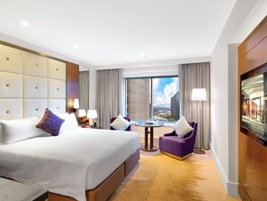 A hotel room with a large bed, a small table, two armchairs, a TV, and a view of the city. - Amora Hotel Jamison Sydney (Sydney)