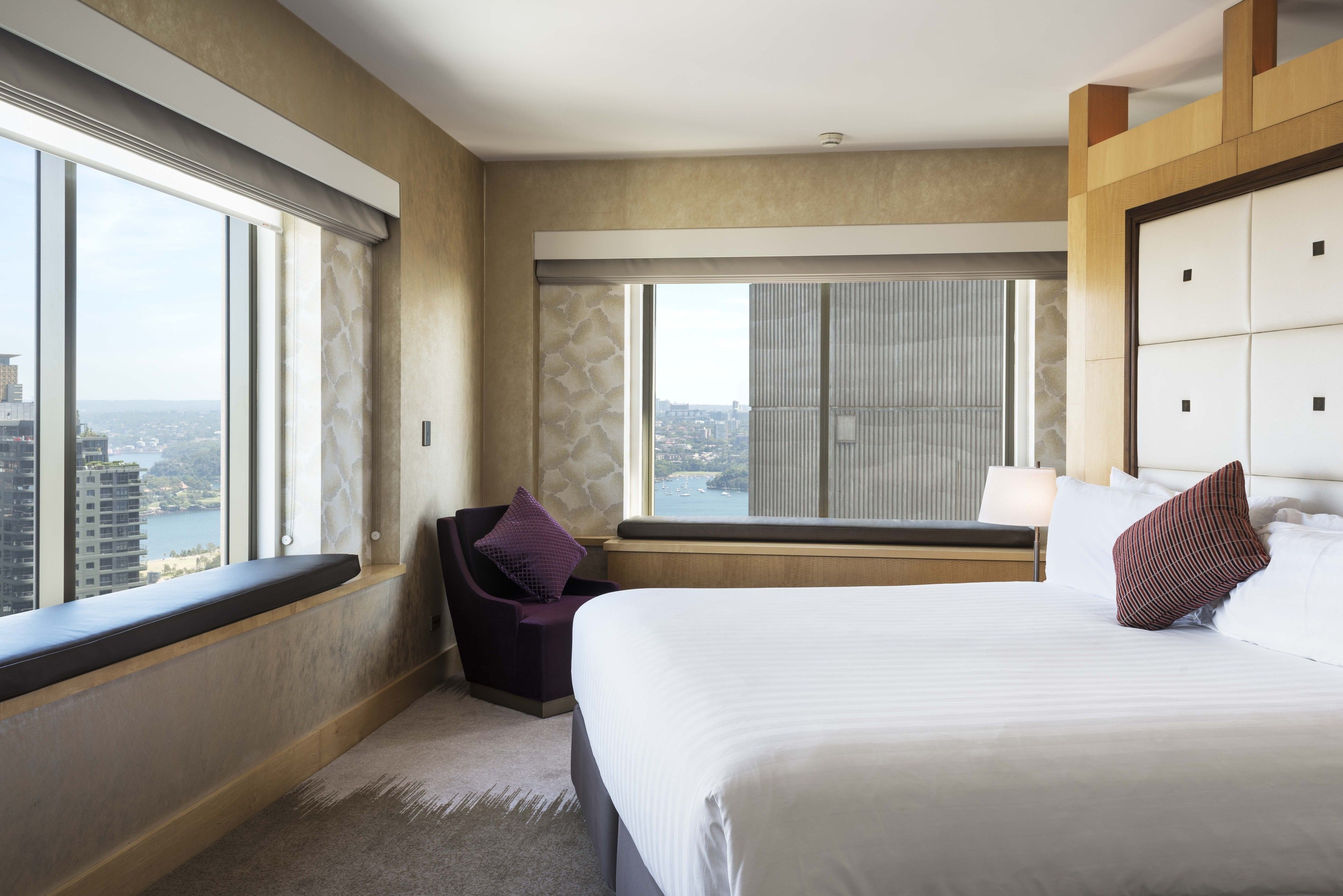 A hotel room with a large bed, a window seat, and a view of the city.