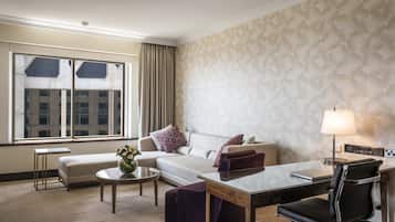 A hotel room with a sofa, a desk, a chair, a coffee table, and a lamp.