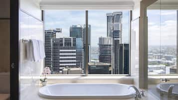 A modern bathroom with a large bathtub, a glass shower enclosure, and a view of a cityscape through large windows.