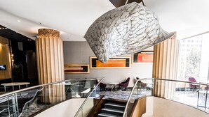 Un interior de varios niveles con una escalera central, barandillas de cristal y una lámpara moderna.
