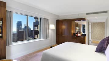 Una habitación de hotel con un ventanal grande, una cama, un armario, un tocador y un baño.