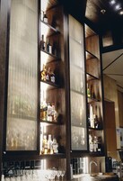 Una zona de bar con estantes de madera que exhiben diferentes botellas y vasos.