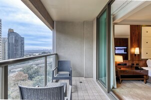 A balcony with a view of a cityscape, a chair, a small table, and a television in a hotel room.