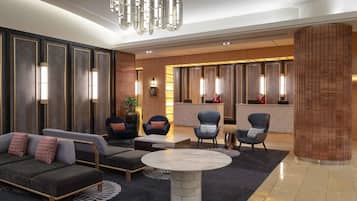 A modern lobby with a sofa, armchairs, a round table, and a reception desk.