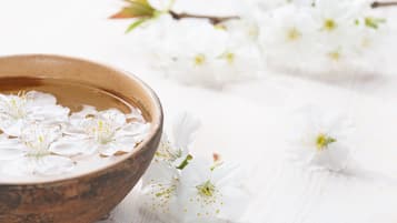Un cuenco de madera lleno de agua y flores blancas sobre una superficie de madera blanca.