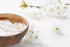 A wooden bowl filled with water and white flowers on a white wooden surface. - Amora Hotel Jamison Sydney (Sydney)
