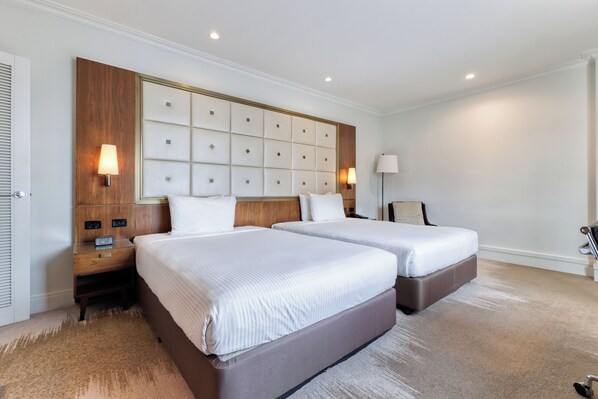 Une chambre d’hôtel avec deux lits, une tête de lit en bois, des tables de chevet et une lampe.