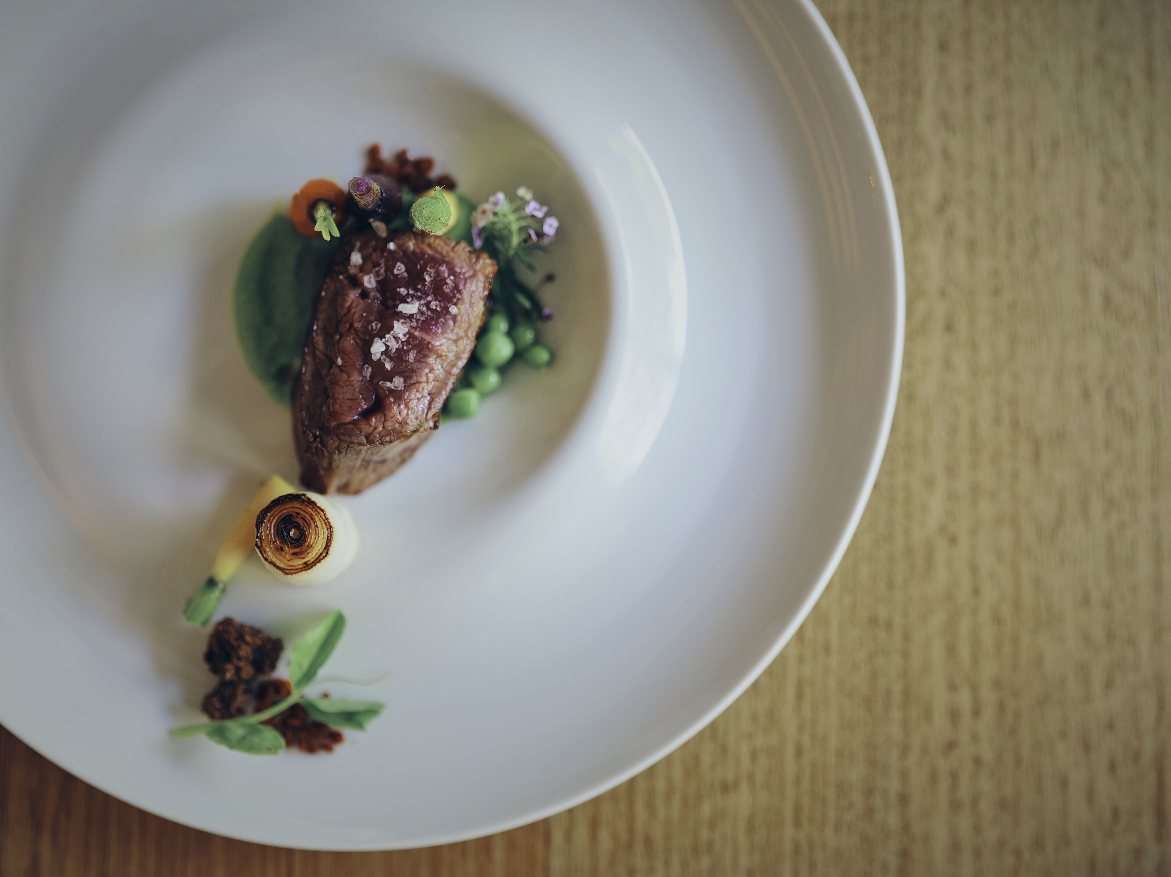 A white plate with a piece of meat, green vegetables, and a small decorative item.