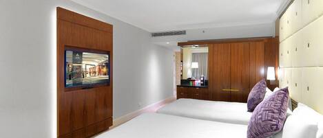 A hotel room with two beds, a wooden wardrobe, a television, and a mirror.