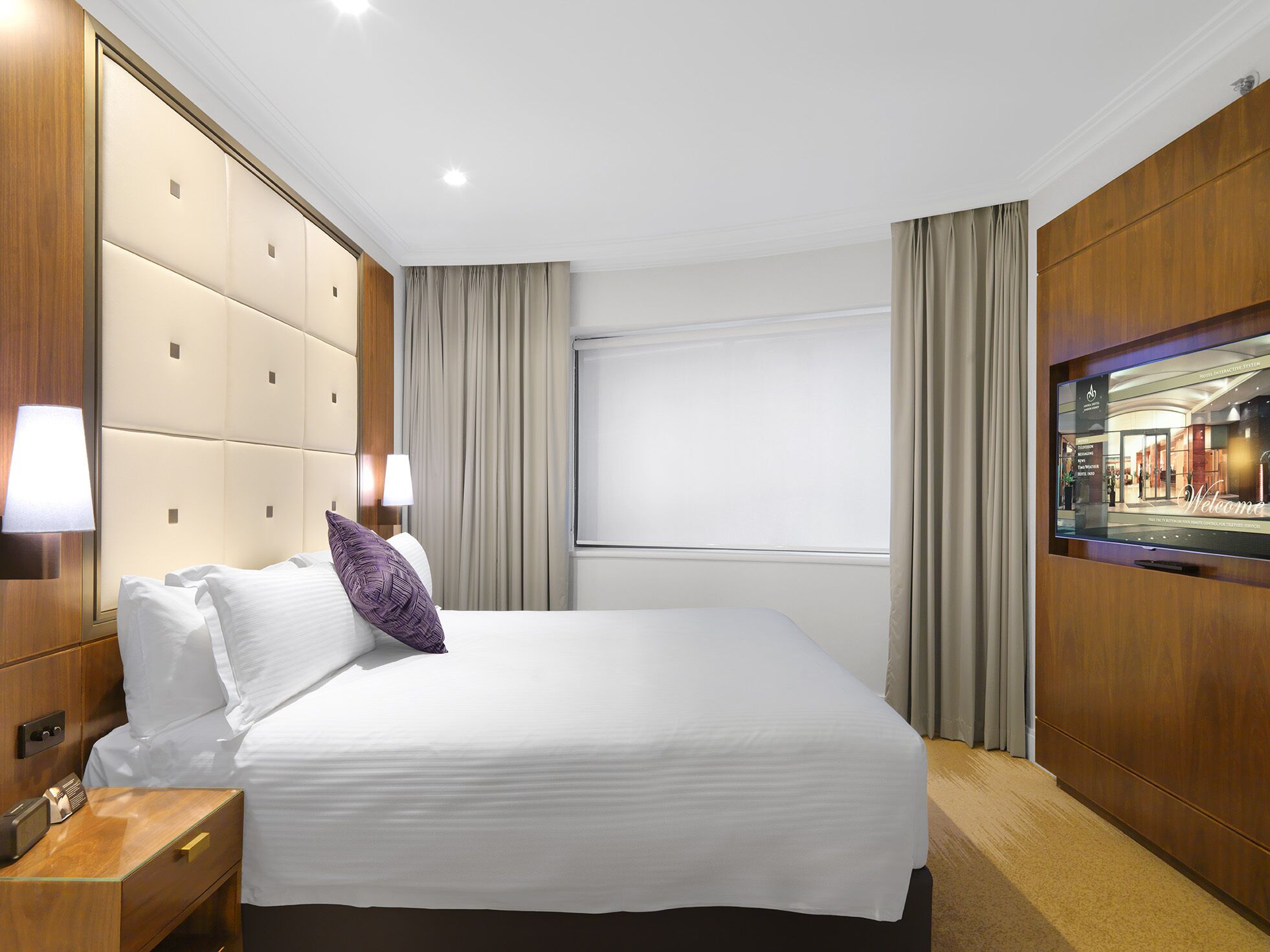 Une chambre d’hôtel avec un grand lit, une table de chevet, une télévision et une fenêtre avec des rideaux.