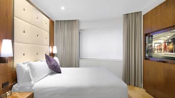 Una habitación de hotel con una cama grande, una mesita de noche, un televisor y un ventanal con cortinas.