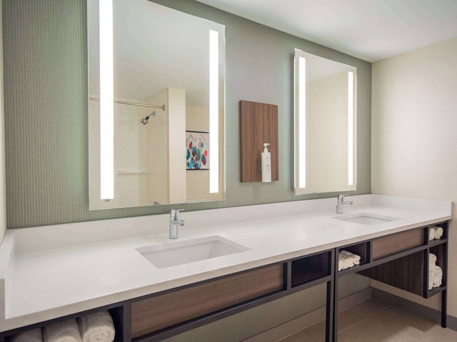 A modern bathroom with a double sink vanity, a large mirror, and built-in shelves for towels.