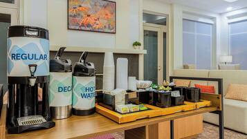 Habitación de hotel con área de kitchenette que incluye cafetera, botellas de licor y dispensador de agua caliente.