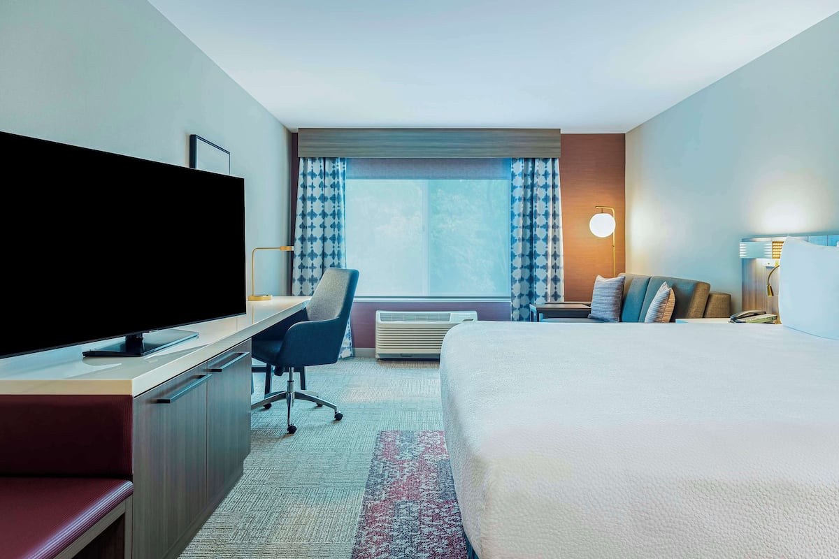 A hotel room with a bed, desk, chair, TV, and a window with curtains.