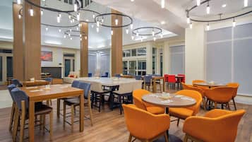 A spacious dining area with multiple tables and chairs, featuring a modern design with wooden floors and ceiling lights.