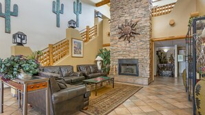 A spacious living area with a stone fireplace, leather sofas, and a wooden staircase. - Best Western Gold Canyon Inn & Suites (Gold Canyon)