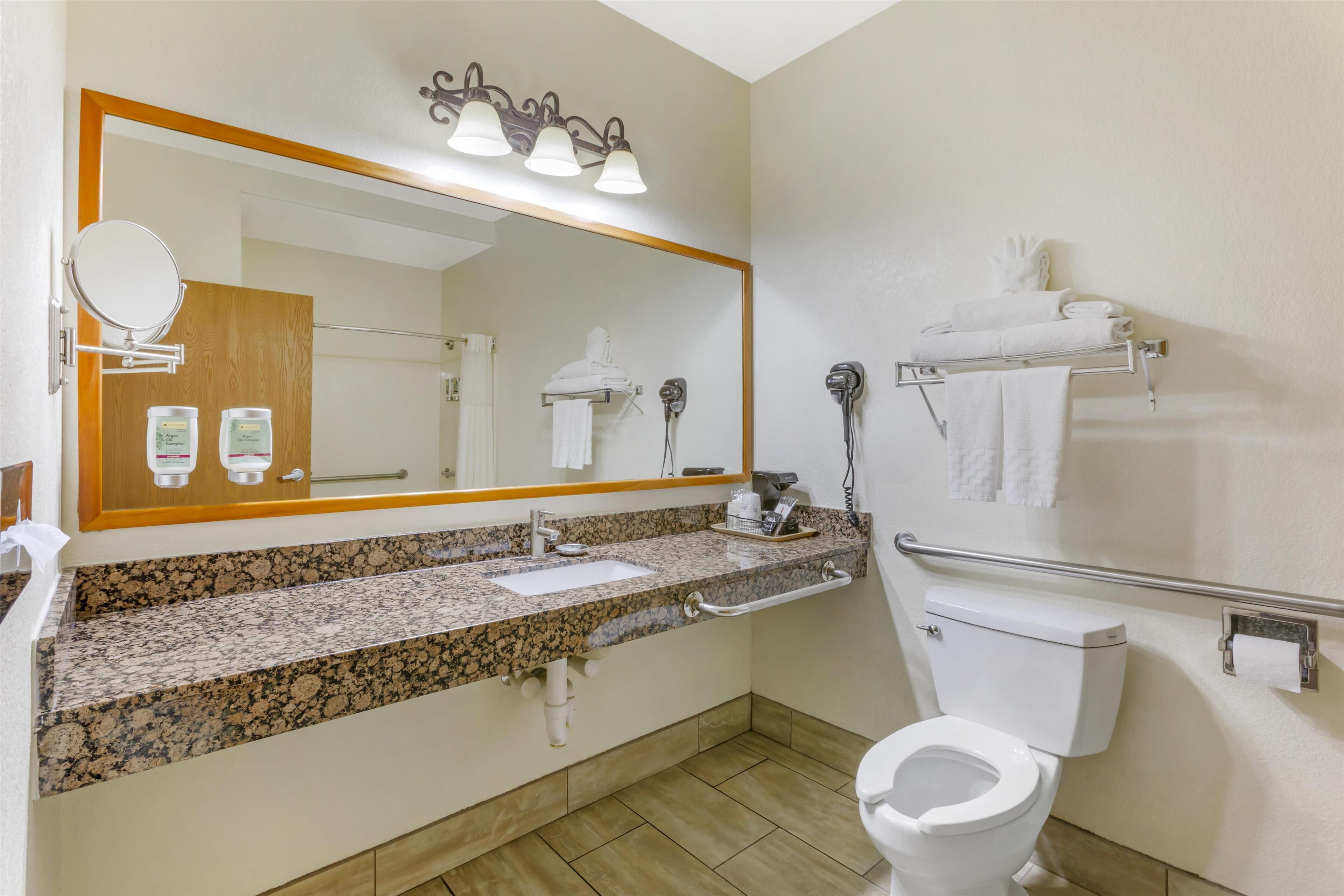 A bathroom with a granite countertop sink, a mirror, a toilet, and a towel rack.