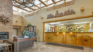 A spacious lobby with a high ceiling, a stone wall, a fireplace, a reception desk with wooden accents, and a wall-mounted clock. - Best Western Gold Canyon Inn & Suites (Gold Canyon)
