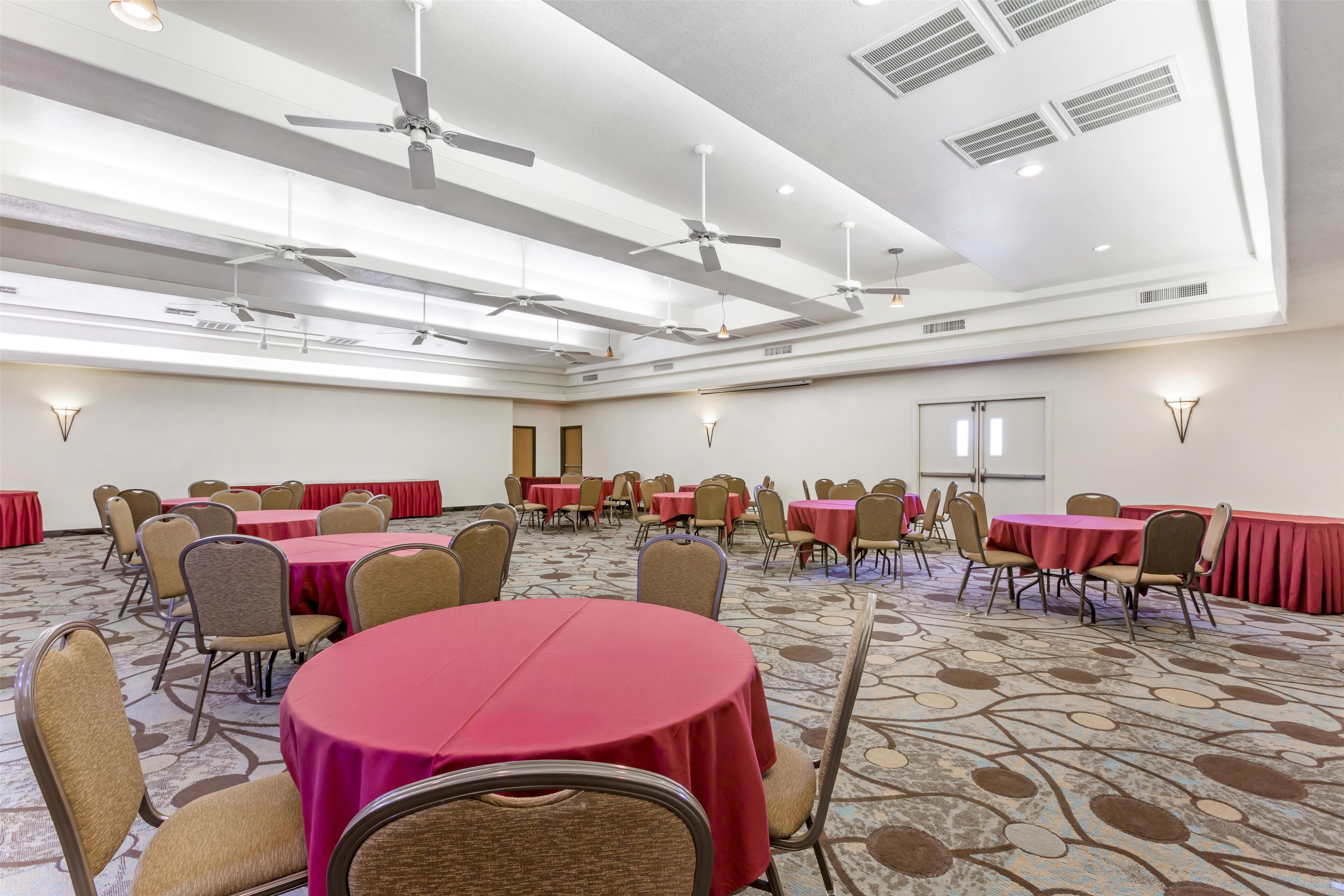 A conference room with multiple tables and chairs, ceiling fans, and recessed lighting.