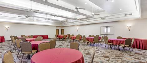 A conference room with multiple tables and chairs, ceiling fans, and recessed lighting.