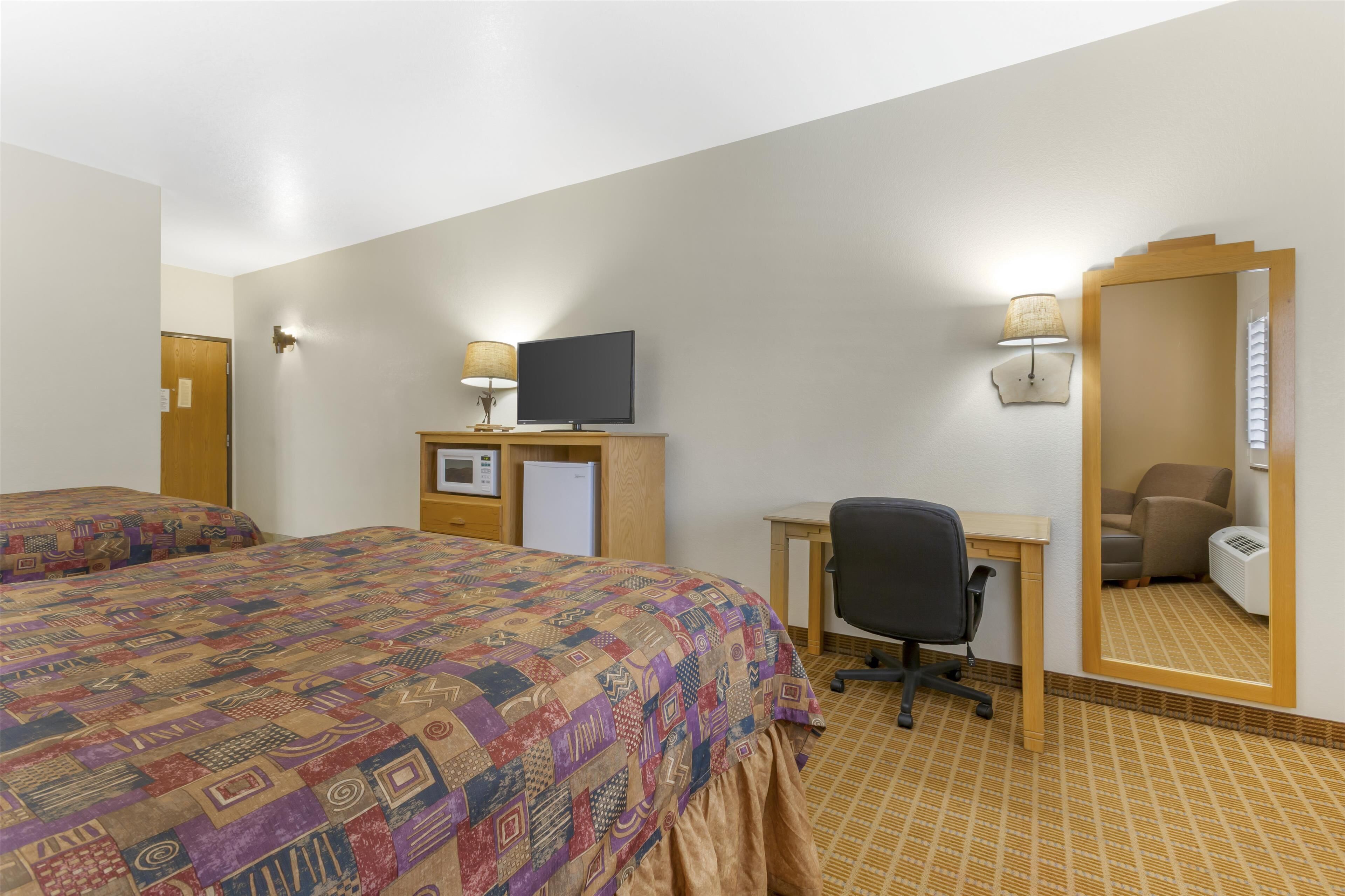 A hotel room with two beds, a desk with a computer, a TV, a mirror, and a lamp.