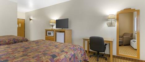 A hotel room with two beds, a desk with a computer, a TV, a mirror, and a lamp.