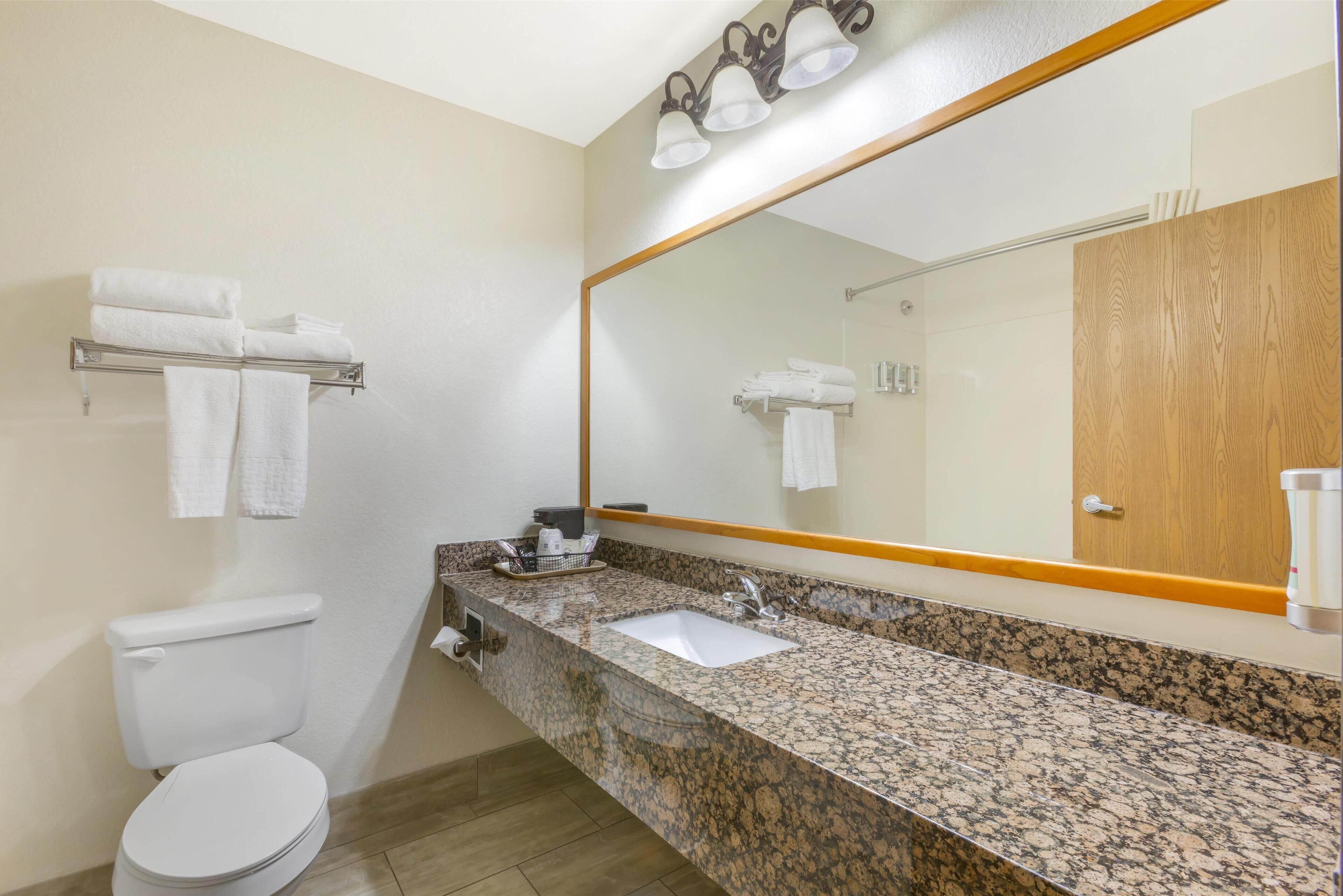 A bathroom with a toilet, sink, and mirror. There are towels on a rack and a wooden door.
