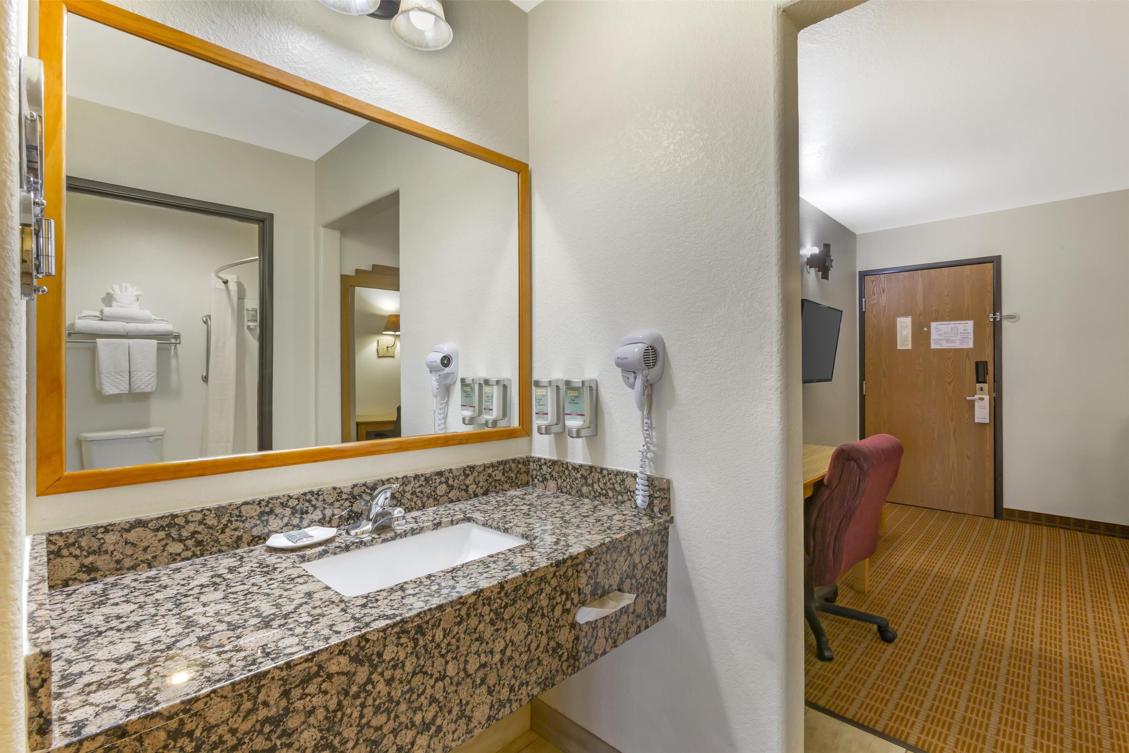 A bathroom with a granite countertop sink, a mirror, a towel rack, and a shower area visible through the door.