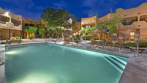A swimming pool with lounge chairs and umbrellas, surrounded by buildings with balconies and greenery. - Best Western Gold Canyon Inn & Suites (Gold Canyon)