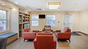 A modern living room with orange sofas, a coffee table, and a bookshelf filled with books and magazines. - MainStay Suites Mt. Laurel - Philadelphia (Mount Laurel)